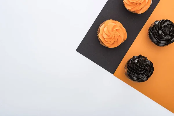 Vista superior de deliciosos cupcakes de Halloween sobre fondo negro, naranja y blanco con espacio para copiar - foto de stock