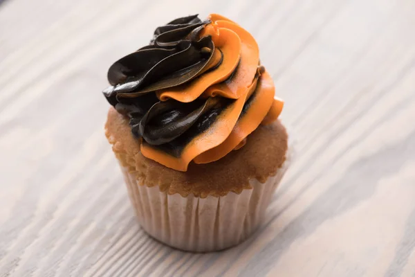 Black and orange delicious Halloween cupcake on wooden table — Stock Photo
