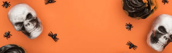 Вид сверху на кексы, декоративные черепа и пауков на оранжевом фоне с копировальным пространством, панорамный снимок — стоковое фото