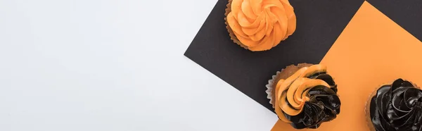 Draufsicht auf köstliche Halloween-Cupcakes auf schwarzem, orangefarbenem und weißem Hintergrund mit Kopierraum, Panoramaaufnahme — Stockfoto