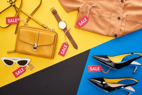 Vue du dessus des vêtements, chaussures et accessoires avec étiquettes de vente sur fond bleu, jaune et noir — Photo de stock