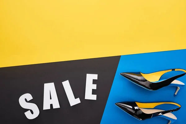Draufsicht auf Verkauf Schriftzug in der Nähe von Schuhen auf blauem, gelbem und schwarzem Hintergrund — Stockfoto