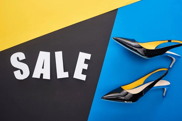 Top view of sale lettering near shoes on blue, yellow and black background — Stock Photo