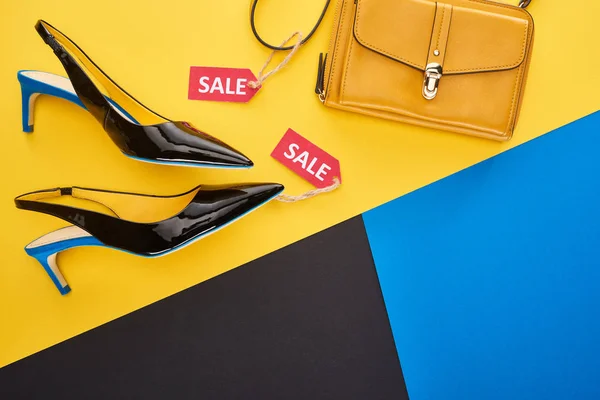 Top view of shoes and bag with sale label on blue, yellow and black background — Stock Photo