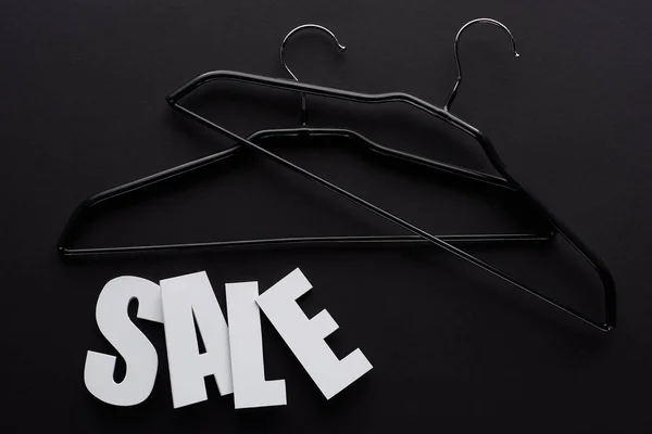 Vista superior de lettering venda branca com cabides no fundo preto — Fotografia de Stock