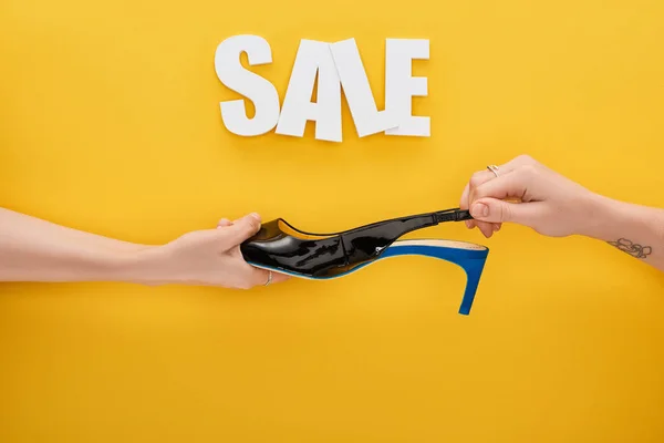 Vista recortada de las mujeres que sostienen el zapato en venta con letras sobre fondo amarillo - foto de stock