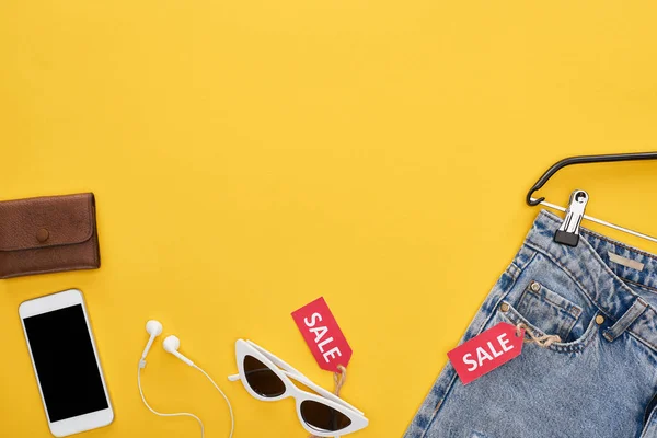 Vista superior de roupas e acessórios da moda com etiquetas de smartphone e venda no fundo amarelo — Fotografia de Stock