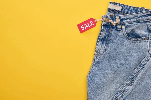 Top view of jeans with sale label on yellow background — Stock Photo