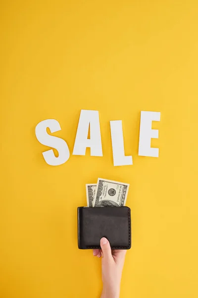 Partial view of woman holding wallet with dollars on yellow background with sale lettering — Stock Photo