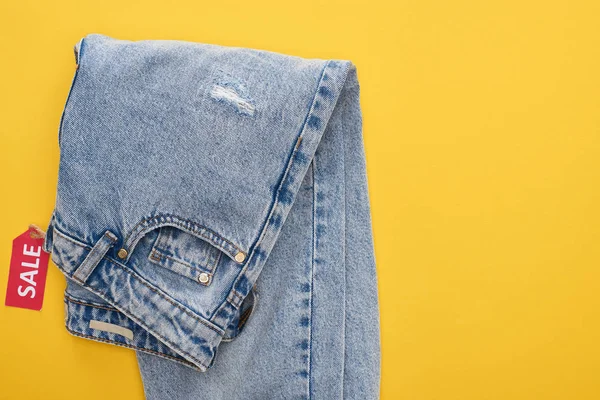 Top view of jeans with sale label on yellow background — Stock Photo