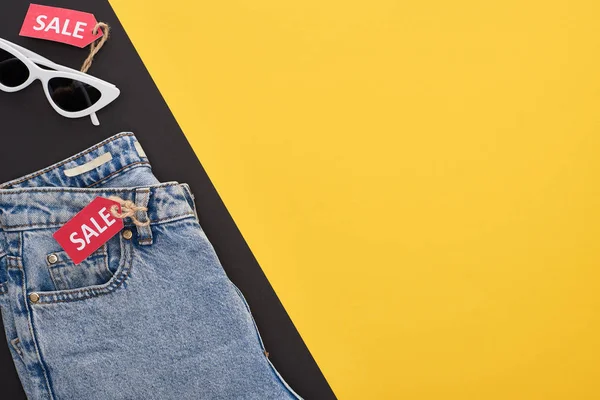Top view of jeans and glasses with sale labels on yellow and black background — Stock Photo