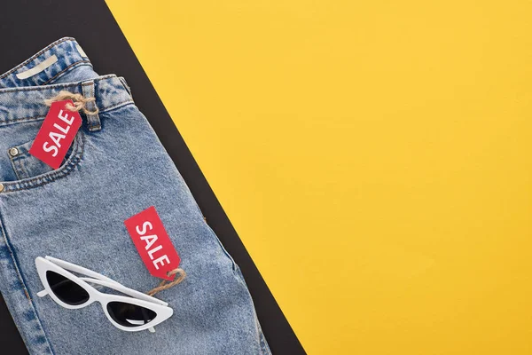 Top view of jeans and glasses with sale labels on yellow and black background — Stock Photo