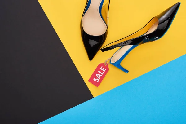 Top view of elegant shoes with sale label on blue, yellow and black background — Stock Photo