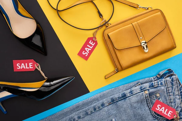 Vista superior de jeans, sapatos e saco com etiquetas de venda em fundo azul, amarelo e preto — Fotografia de Stock