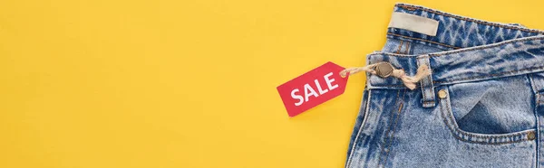 Top view of jeans with sale label isolated on yellow — Stock Photo