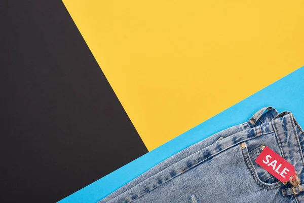 Vue du haut des jeans avec étiquette de vente sur fond bleu, jaune et noir — Photo de stock