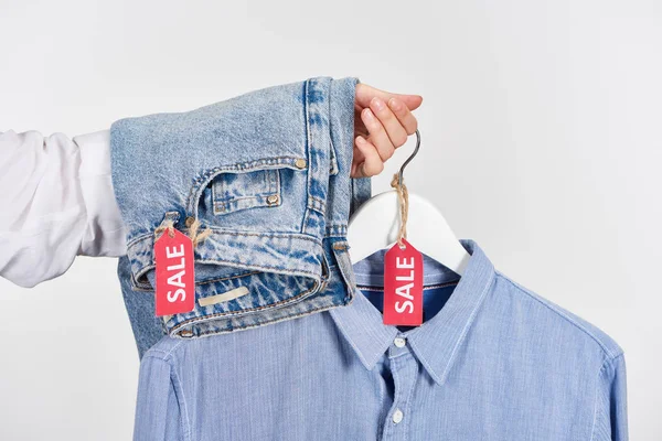 Vue recadrée de femme tenant jeans et chemise avec des étiquettes de vente isolées sur blanc — Photo de stock