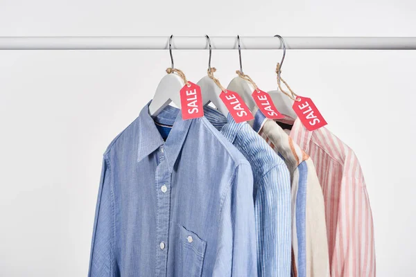 Elegantes camisas colgando con etiquetas de venta aisladas en blanco - foto de stock