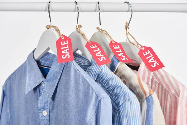 Elegantes camisas colgando con etiquetas de venta aisladas en blanco - foto de stock