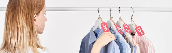 Blonde woman near elegant shirts hanging with sale labels isolated on white, panoramic shot — Stock Photo