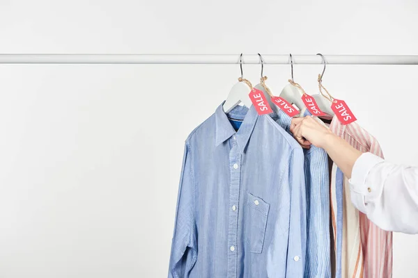 Vista cortada da mulher perto de camisas elegantes penduradas com etiquetas de venda isoladas em branco — Fotografia de Stock