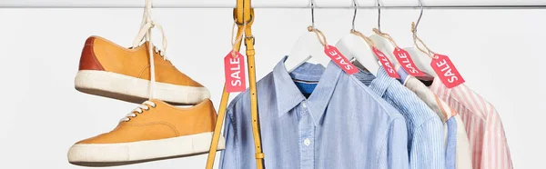 Zapatillas de deporte, bolso y camisas elegantes colgando con etiquetas de venta aisladas en blanco, plano panorámico - foto de stock