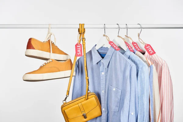 Sapatilhas, bolsa e camisas elegantes penduradas com etiquetas de venda isoladas em branco — Fotografia de Stock