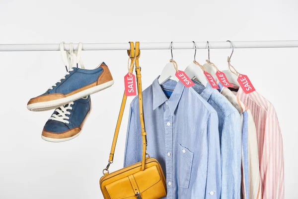 Sapatilhas, bolsa e camisas elegantes penduradas com etiquetas de venda isoladas em branco — Fotografia de Stock