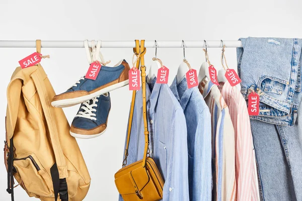 Calzado, accesorios y camisas elegantes colgando con etiquetas de venta aisladas en blanco - foto de stock