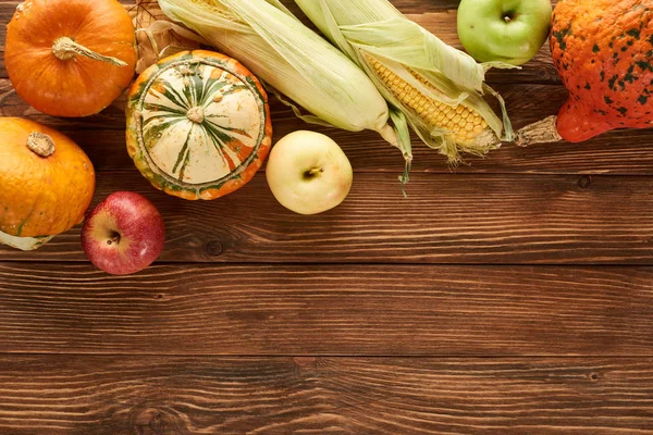 Vista dall'alto di mais dolce crudo, zucche e mele su una superficie di legno marrone — Foto stock