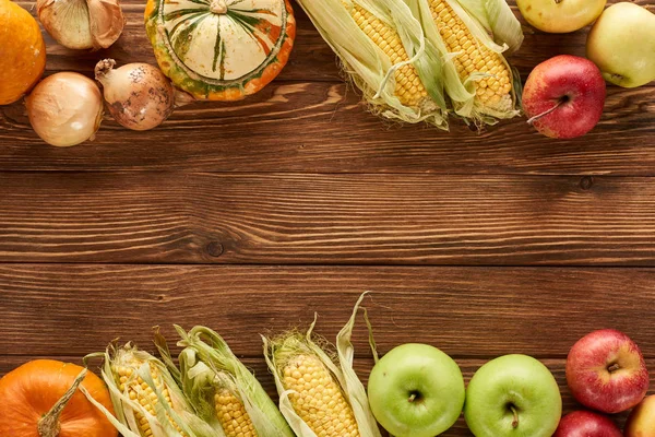 Top view of raw sweet corn, pumpkins, onions and apples on brown wooden surface — Stock Photo