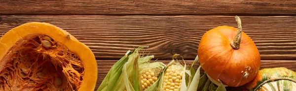 Panoramic shot of raw sweet corn, whole and half of pumpkin on brown wooden surface — Stock Photo