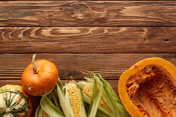 Top view of raw sweet corn, whole pumpkin and half on brown wooden surface — Stock Photo