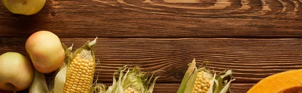 Panoramic shot of raw sweet corn and apples on brown wooden surface — Stock Photo
