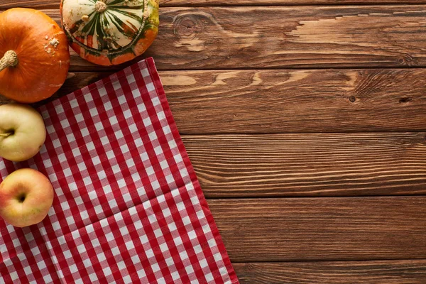 Vue de dessus de la nappe à carreaux avec des pommes fraîches et des citrouilles sur la surface en bois avec espace de copie — Photo de stock