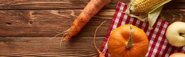 Plan panoramique de nappe à carreaux avec citrouille, maïs doux, pommes et carottes sur la surface en bois avec espace de copie — Photo de stock