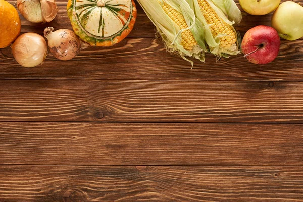 Vista superior de maíz dulce crudo, cebollas, calabazas y manzanas en la superficie de madera marrón - foto de stock