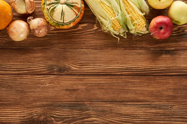 Top view of raw sweet corn, onions, pumpkins and apples on brown wooden surface — Stock Photo