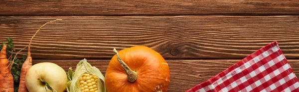 Plan panoramique de nappe à carreaux près de la citrouille, du maïs sucré, des pommes et des carottes sur une surface en bois avec espace de copie — Photo de stock