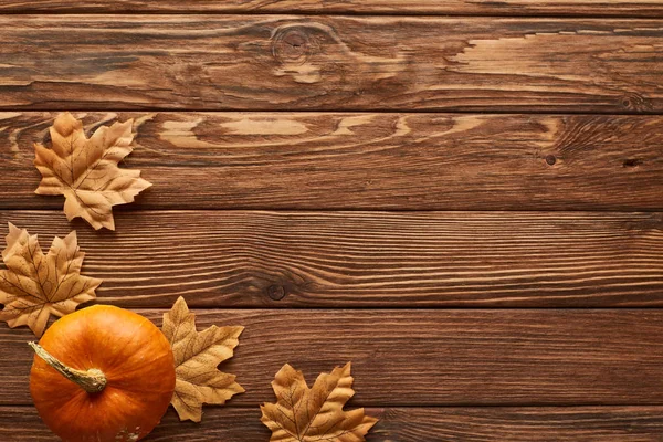 Vista superior de abóbora pequena na superfície de madeira marrom com folhas de outono secas — Fotografia de Stock