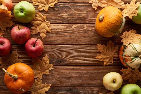 Top view of pumpkins and apples on brown wooden surface with dried autumn leaves — Stock Photo