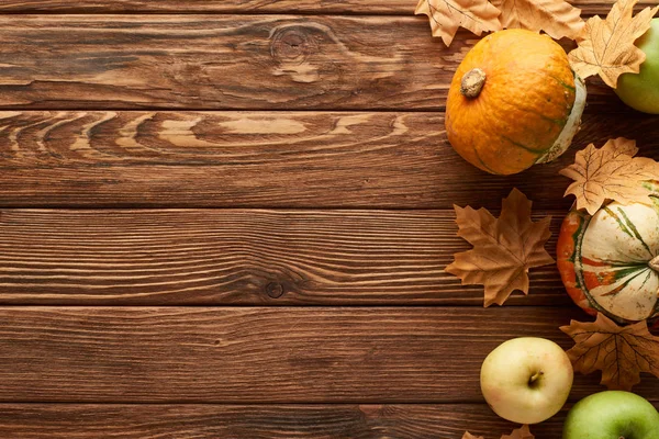 Top view of pumpkins and apples on brown wooden surface with dried autumn leaves and copy space — Stock Photo