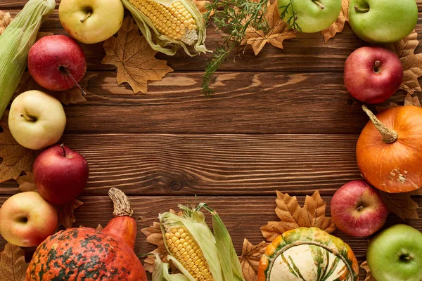 Vista superior do quadro de abóboras, milho doce e maçãs na superfície de madeira com folhas de outono secas — Fotografia de Stock