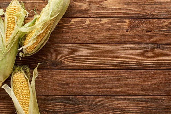 Top view of uncooked sweet corn on brown wooden surface — Stock Photo