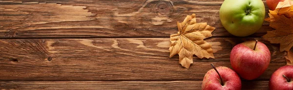 Plan panoramique de pommes diverses sur une surface en bois avec des feuilles séchées — Photo de stock