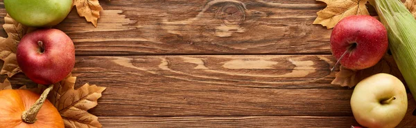 Colpo panoramico di zucche mature, mais dolce e mele dolci su superficie di legno con foglie secche — Foto stock