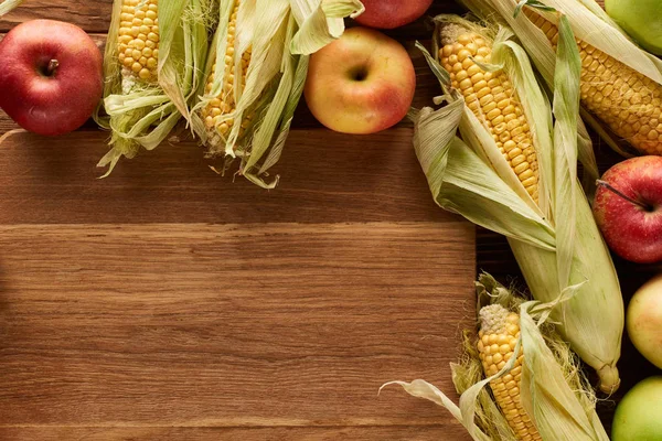 Top view of uncooked sweet corn and ripe apples on wooden surface with copy space — Stock Photo