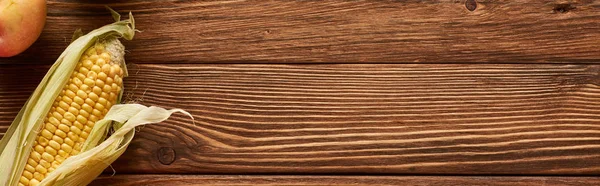 Панорамный снимок спелой сладкой кукурузы и яблока на коричневой деревянной поверхности — стоковое фото