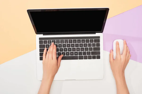 Обрезанный вид женщины с помощью ноутбука и компьютерной мыши на бежевом, фиолетовом и белом фоне — стоковое фото
