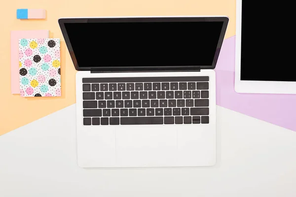 Top view of laptop with blank screen, digital tablet and office supplies on beige, violet and white background — Stock Photo